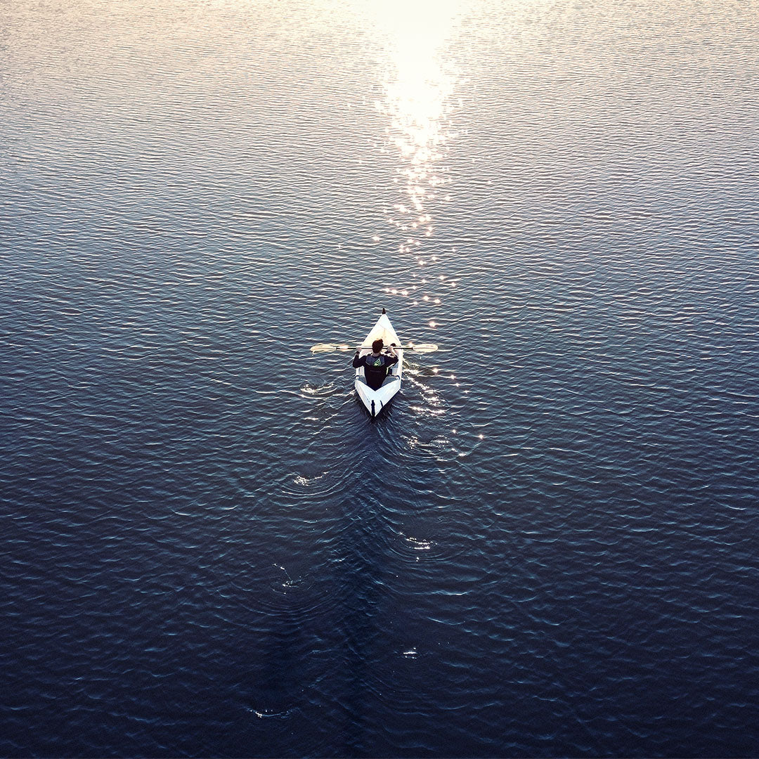 Man rowing origami canoe, MyCanoe Solo 2, on blue water towards the sunrise